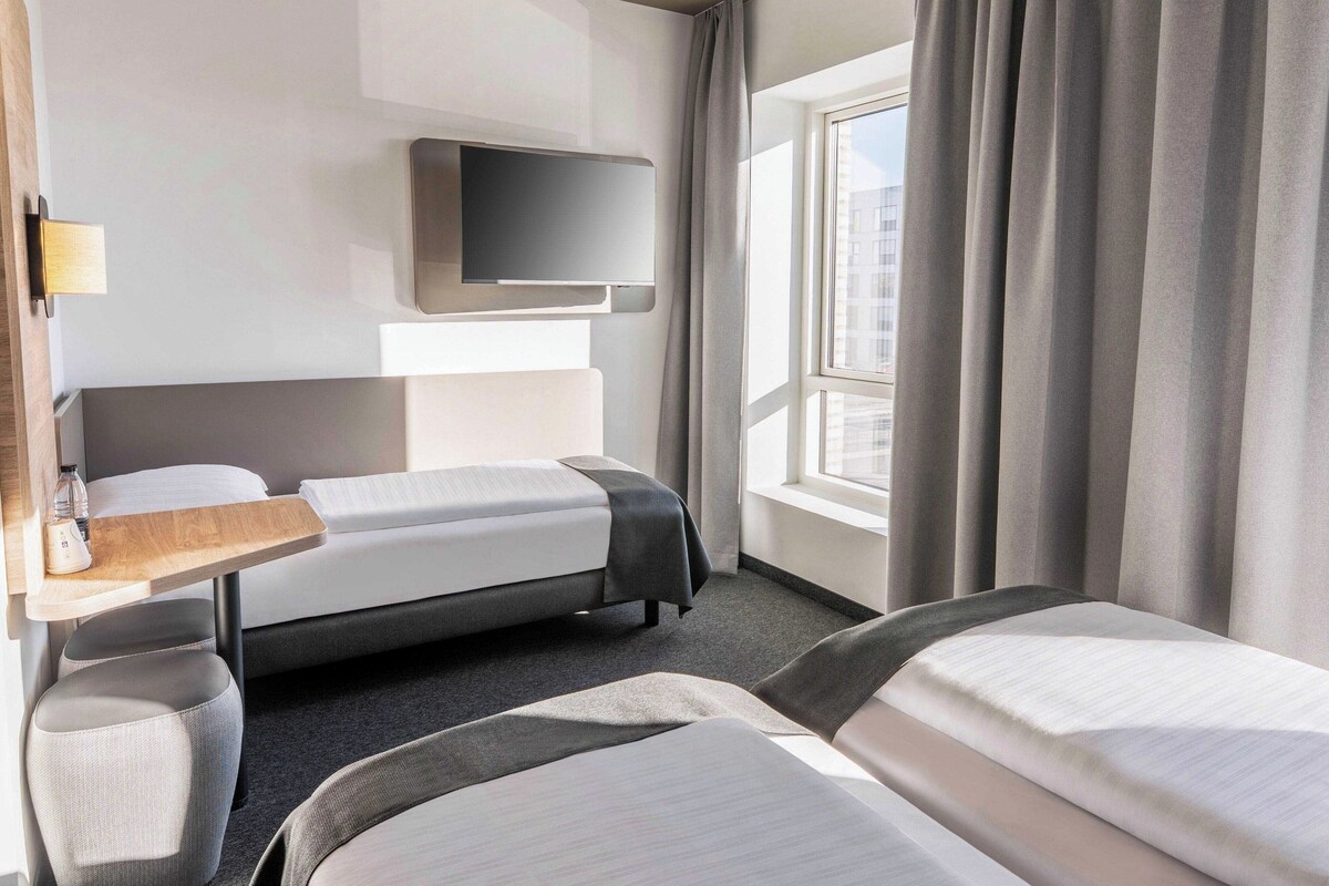 A hotel room with a bed, a desk, a TV, and a window with curtains.