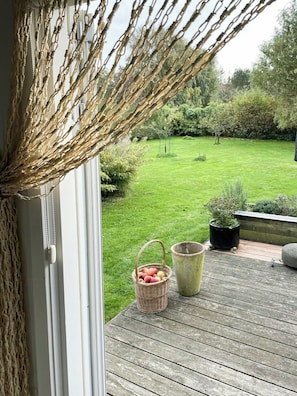 Une terrasse en bois avec un panier en osier rempli de fruits, une plante en pot et une vue sur un jardin verdoyant.