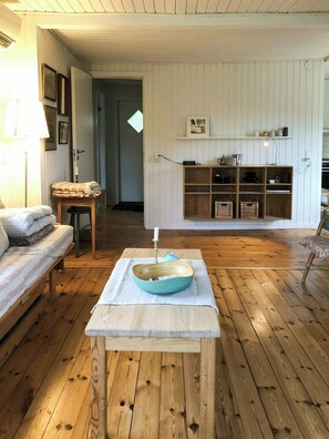 Ein Zimmer mit Holzboden, einer Couch, einem Tisch mit einer Schüssel und einem Regal mit verschiedenen Gegenständen.