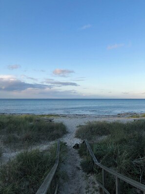 Ein Strandweg, der zum Meer führt, mit einem Holzzaun und grasbewachsenen Dünen.