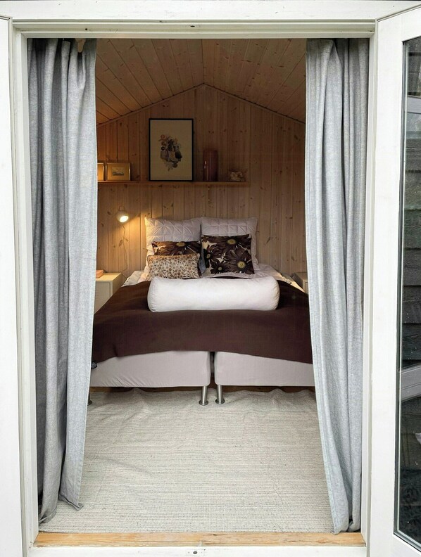 Een knus slaapkamer met een bed, gordijnen, een lamp en een ingelijst foto aan de muur.