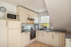 A modern kitchen with white cabinets, a microwave, a stove, and a window with a view of greenery. - Koch Holiday Apartment up to 100m² with Balcony in Bad Grund (Bad Grund (Harz))