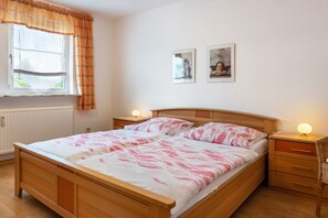 A bedroom with a wooden bed, two bedside tables, a window with curtains, and two framed pictures on the wall. - Koch Holiday Apartment up to 100m² with Balcony in Bad Grund (Bad Grund (Harz))