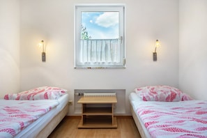 Een kamer met twee bedden, een raam met uitzicht op bomen en wandlampen.