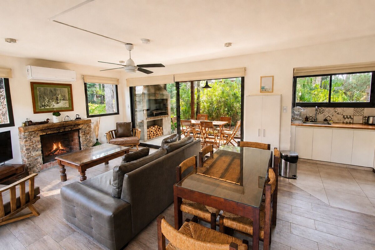 Amplia sala de estar con chimenea, asientos cómodos, una mesa de comedor y una cocina con ventanas amplias.