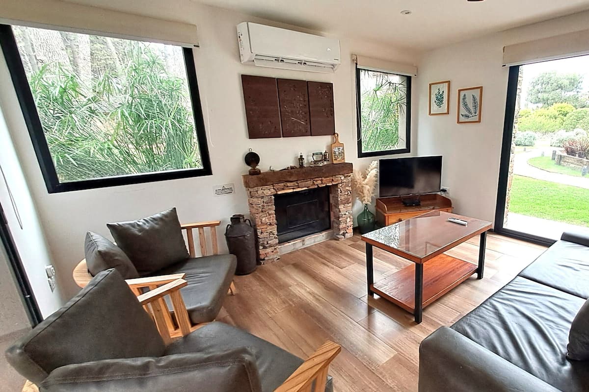Una sala de estar con chimenea, televisor y un ventanal con vistas al verdor.