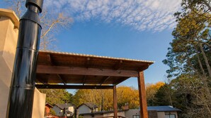 An outdoor patio with a wooden table and chairs, a pergola, and a black chimney. - Complejo Playa Bonita Mar Azul 100m playa (Mar Azul)