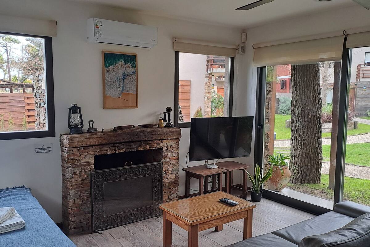 Una sala de estar con chimenea de piedra, un televisor de pantalla plana, un sofá, una mesa de centro y vistas al exterior.