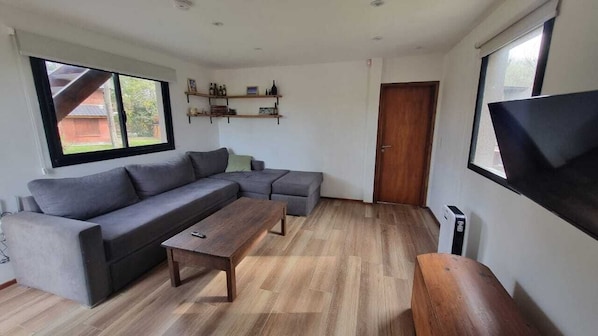 A living room with a sectional sofa, a wooden coffee table, and a flat-screen TV mounted on the wall.
