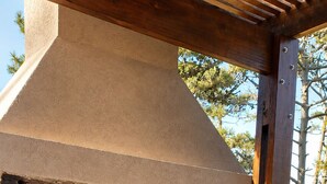 Un horno de ladrillo al aire libre con techo de madera, un banco y una pila de leña.