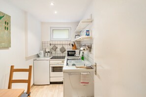 A compact kitchen with a refrigerator, stove, microwave, and sink. There is a wooden chair and a small table. - Koch Apartment – Quiet Souterrain up to 80 m², Near Bad Grund & Osterode, Sleeps 6 (Bad Grund)