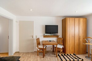 A compact living space with a wooden wardrobe, a television mounted on a shelf, a small table with chairs, and a striped rug. - Koch Apartment – Quiet Souterrain up to 80 m², Near Bad Grund & Osterode, Sleeps 6 (Bad Grund)
