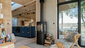 Een modern interieur met een houtkachel, een eethoek met rieten meubels, en een keuken met blauwe kasten.