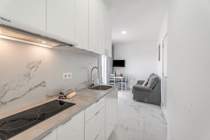 Una cucina moderna con piano cottura integrato, mobili bianchi e una parete di fondo in marmo.