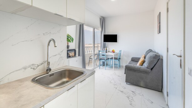 A modern kitchen with a marble countertop and sink, a dining area with blue chairs, and a grey sofa with a TV mounted on the wall. - Vacation Apartment 'Balcón Panorámico, Mar Y Puesta Sol' with Sea View, Balcony and Wi-Fi (Guargacho)