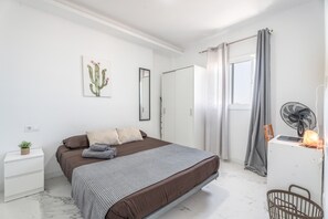Een slaapkamer met een bed, nachtkastje, gordijnen, een ventilator en een raam.