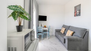 A modern living room with a grey sofa, a dining table with chairs, a potted plant, and a flat-screen TV mounted on the wall. - Vacation Apartment 'Balcón Panorámico, Mar Y Puesta Sol' with Sea View, Balcony and Wi-Fi (Guargacho)