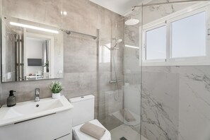 Een moderne badkamer met een douchecabine van glas, een witte wastafel en een grote spiegel.
