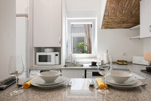 Une cuisine moderne avec des meubles blancs, un four à micro-ondes, un évier et une fenêtre donnant sur un espace verdoyant.