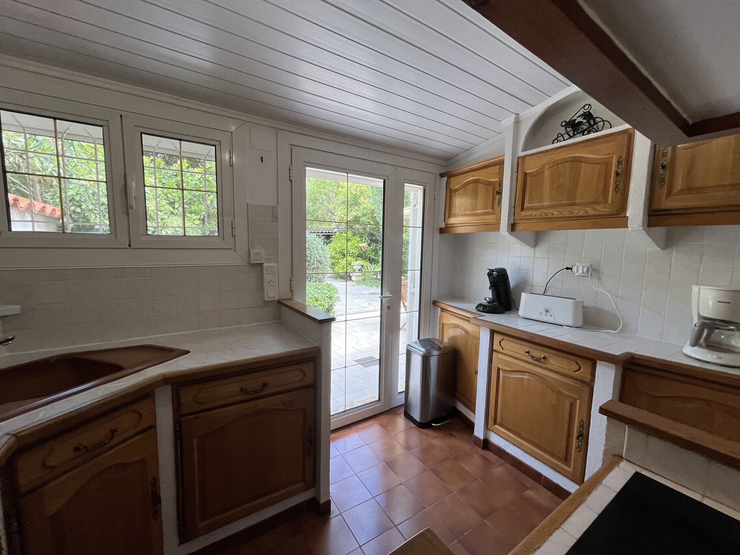 A kitchen with wooden cabinets, a sink, a coffee maker, and a trash bin.
