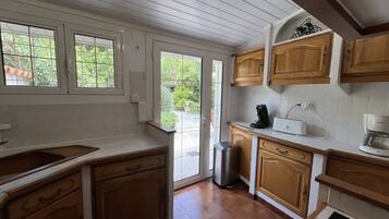 A kitchen with wooden cabinets, a sink, a coffee maker, and a trash bin.