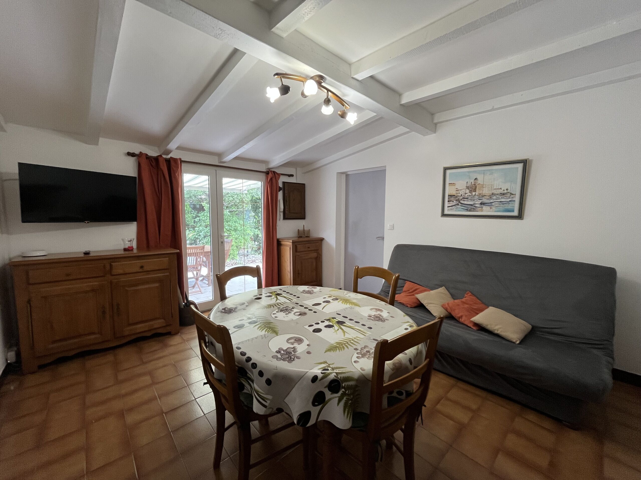 A dining area with a table, chairs, a sofa, a TV, and a door leading to a balcony.