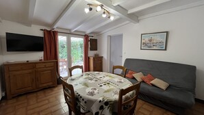 A dining area with a table, chairs, a sofa, a TV, and a door leading to a balcony. - Fréjus Plage - 5-minute walk to the beaches - Small house with garden, sleeps 4, in absolute peace and quiet (Fréjus)