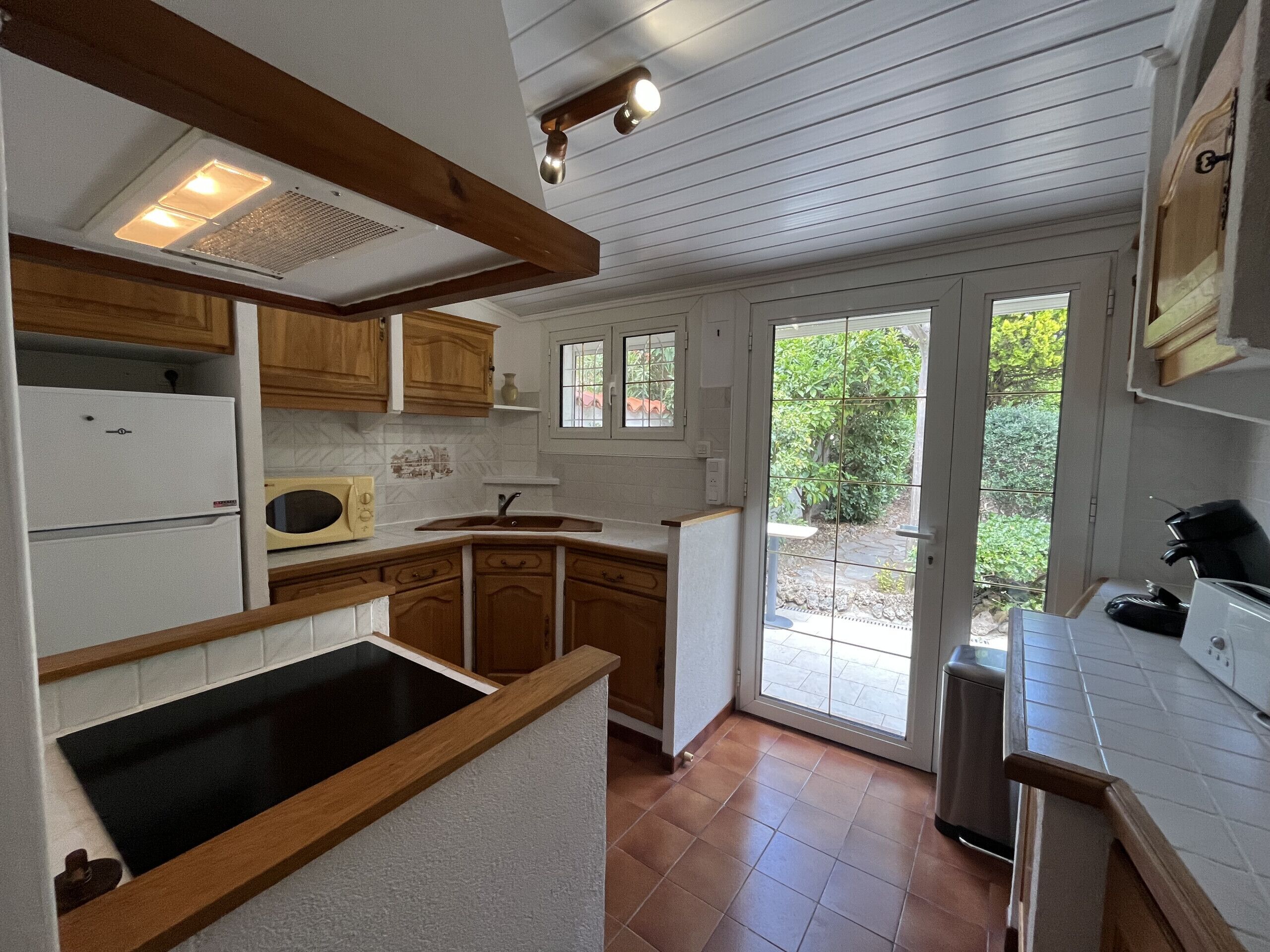 Une cuisine avec des meubles de rangement en bois, un four à micro-ondes encastré, un évier et une fenêtre donnant sur un jardin.