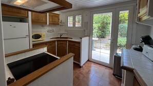 A kitchen with wooden cabinets, a built-in microwave, a sink, and a window overlooking a garden. - Fréjus Plage - 5-minute walk to the beaches - Small house with garden, sleeps 4, in absolute peace and quiet (Fréjus)