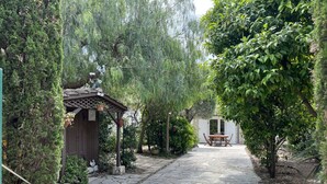 A stone pathway leading to a wooden pergola with a table and chairs, surrounded by lush greenery and a white building in the background. - Fréjus Plage - 5-minute walk to the beaches - Small house with garden, sleeps 4, in absolute peace and quiet (Fréjus)