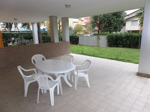 Eine Terrasse im Freien mit einem runden Tisch und sechs Stühlen, umgeben von einer Ziegelmauer und einem Rasen.