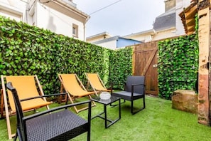 Un patio con mobiliario exterior, una mesa y un muro de seto verde.