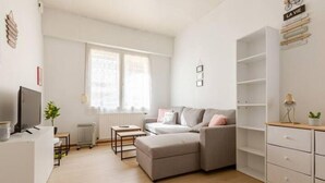 A modern living room with a grey sofa, a small table, a radiator, and a TV.