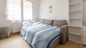 A room with a bed, a sofa, a radiator, and a window with curtains.