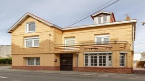 A two-story building with a flat roof, a balcony on the second floor, and a front entrance with a door and windows.