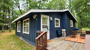 Una cabaña pequeña con terraza, puerta y ventanas.