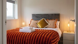 Un letto rifatto con cura, una testiera decorata e una finestra con persiane, con una lampada da comodino su un tavolino.