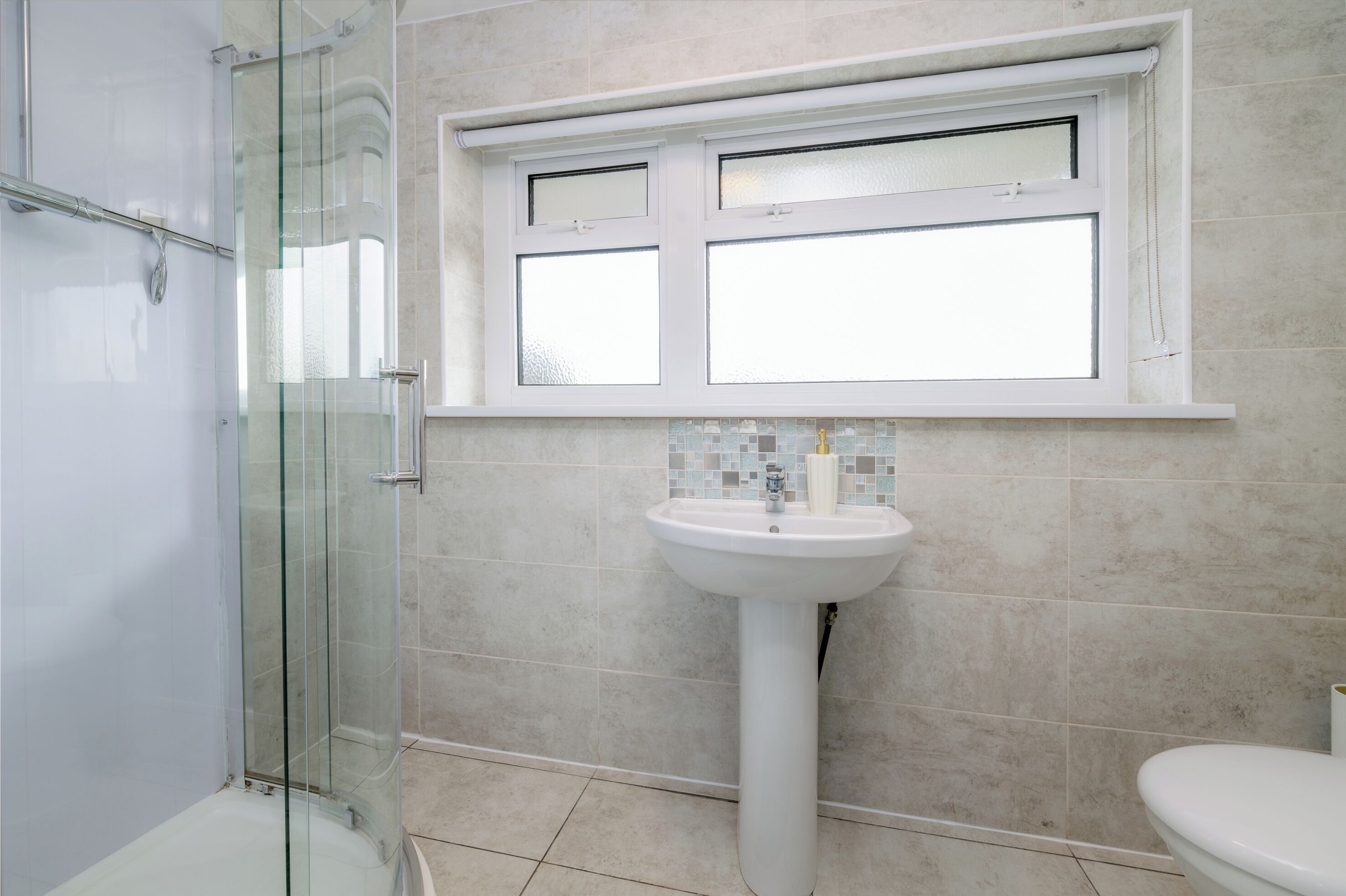 A bathroom with a glass shower enclosure, a pedestal sink, and a toilet.