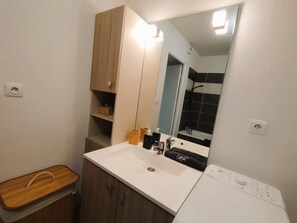 Ein Badezimmer mit einem weißen Waschbecken, einem Holzschrank, einem Spiegel und einem Handtuchhalter.