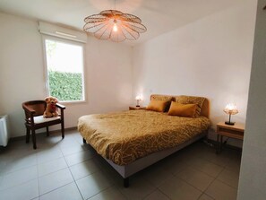 Ein Schlafzimmer mit einem Bett, zwei Nachttischen, einem Sessel, einem Fenster und einer Pendelleuchte.