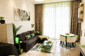 Un salon moderne comprenant un canapé, une table basse en verre, une table à manger avec des chaises et une grande fenêtre avec des rideaux.