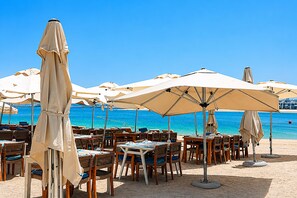 Espace extérieur aménagé avec des parasols, des tables et des chaises, situé sur une plage avec vue sur la mer.