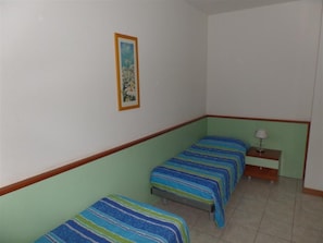 Ein Zimmer mit zwei Einzelbetten, einem Nachttisch mit Lampe und einem gerahmten Bild an der Wand.