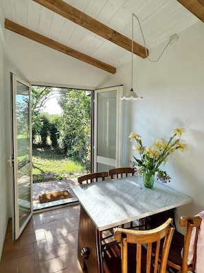 A dining area with a table, chairs, a vase of flowers, and a view of greenery through a glass door. - 1927 house Rome's Appia Antica Park (Roma)