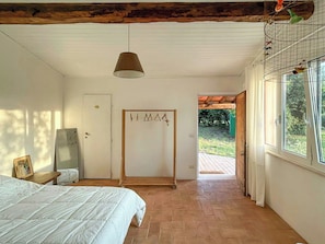 A bedroom with a bed, a hanging lamp, a door with a coat rack, and a window with a view of greenery. - 1927 house Rome's Appia Antica Park (Roma)