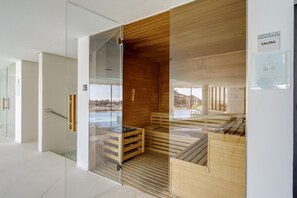 Ein Saunaraum mit Holzbänken und Glaswänden, einer Holzbeschichtung der Decke und Blick ins Freie.