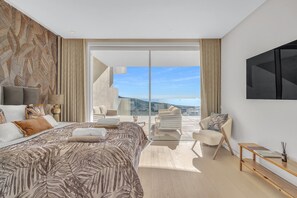 Ein modernes Schlafzimmer mit einem großen Bett, einer Sitzecke mit Sessel und Tisch und einem Balkon mit Aussicht.