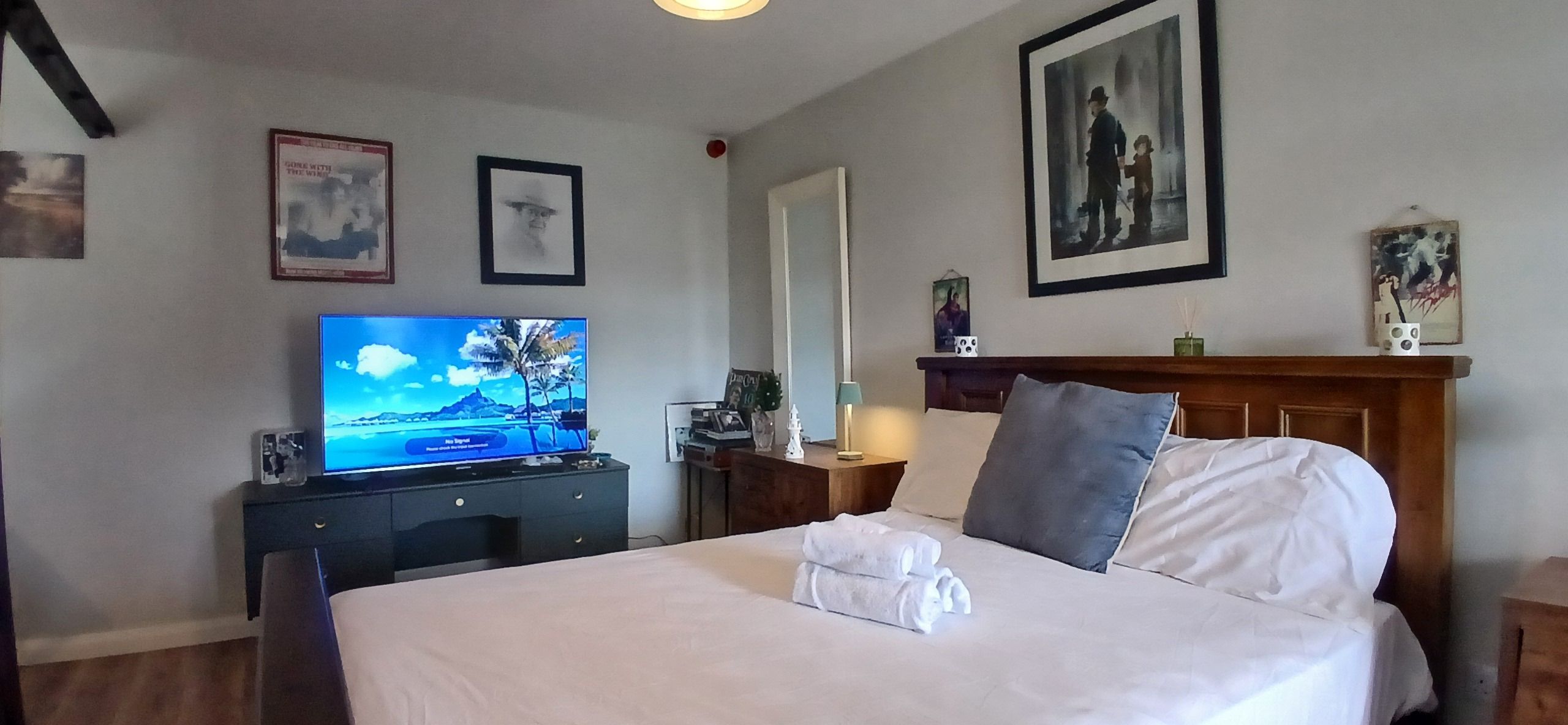 Et hotelværelse med seng, fjernsyn, kommode og billeder på væggene.