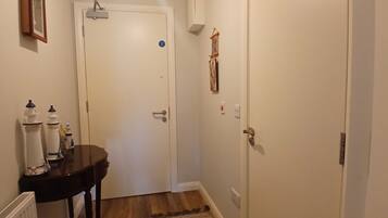 A hallway with a white door, a small table with a plant, and a coat rack.
