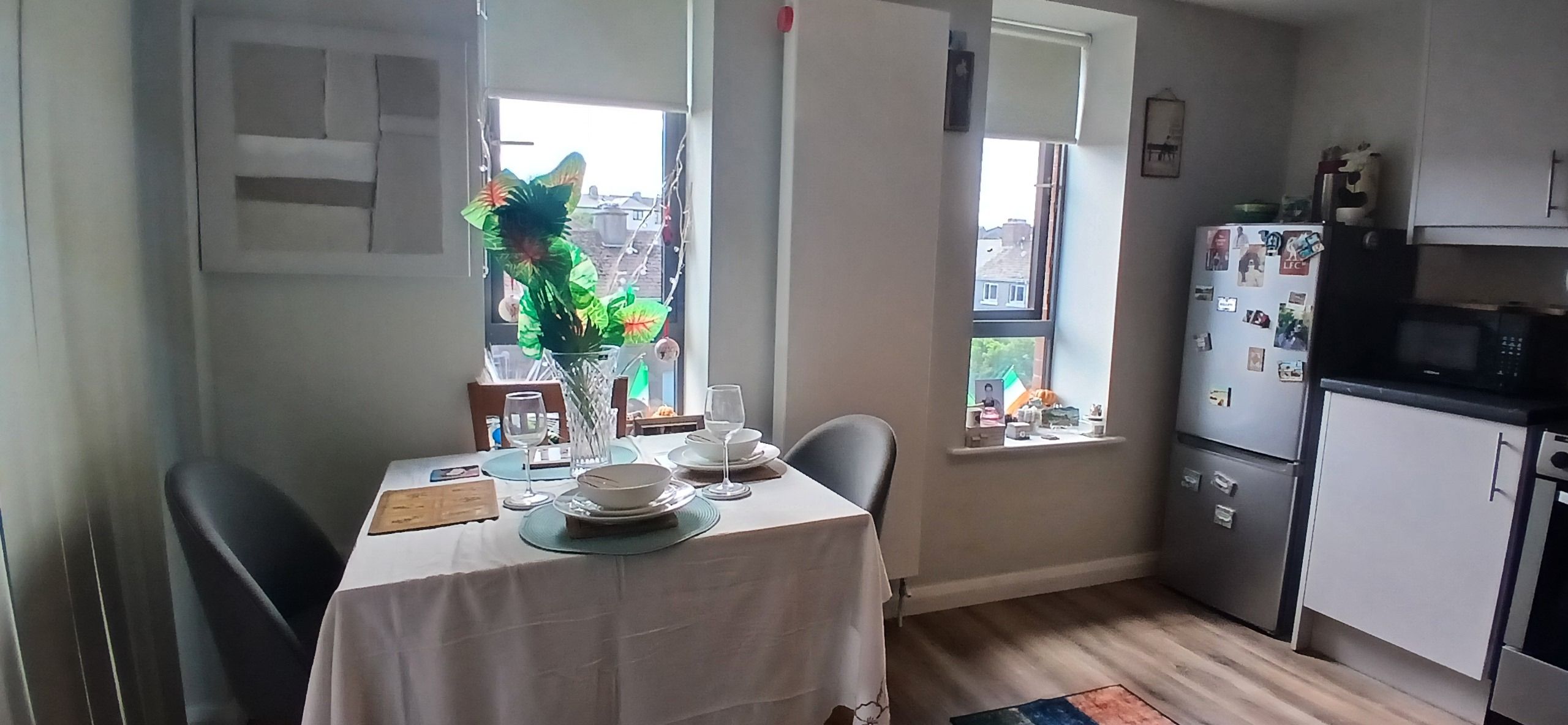 A compact kitchen with a dining table set for two, a refrigerator, and a window with a view of the outside.